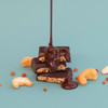Cashew Caramel Crunch 70% Filled Dark Chocolate with chocolate pouring over it with blue background