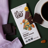 Theo Almond Brittle Crunch 55% Dark Chocolate Bar with cup of coffee on green background